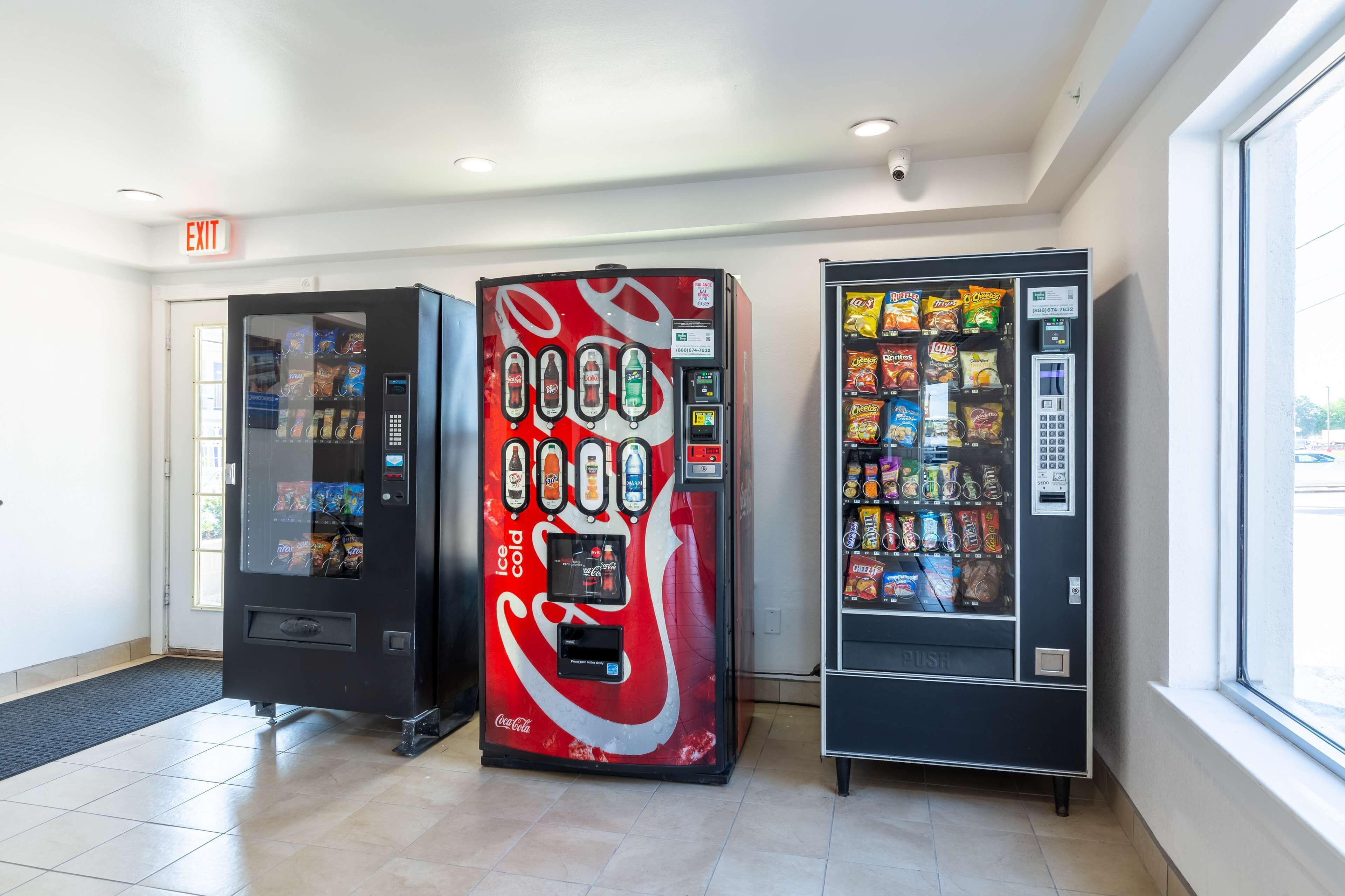 A vending area with a Coca-Cola branded machine, a snack vending machine, and a door with an exit sign.