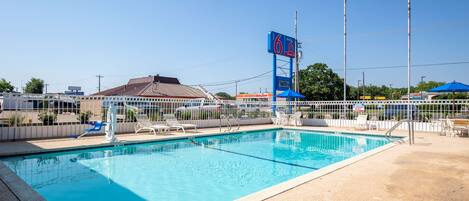 Piscina con área cercada, sillas de descanso y un cielo azul despejado.