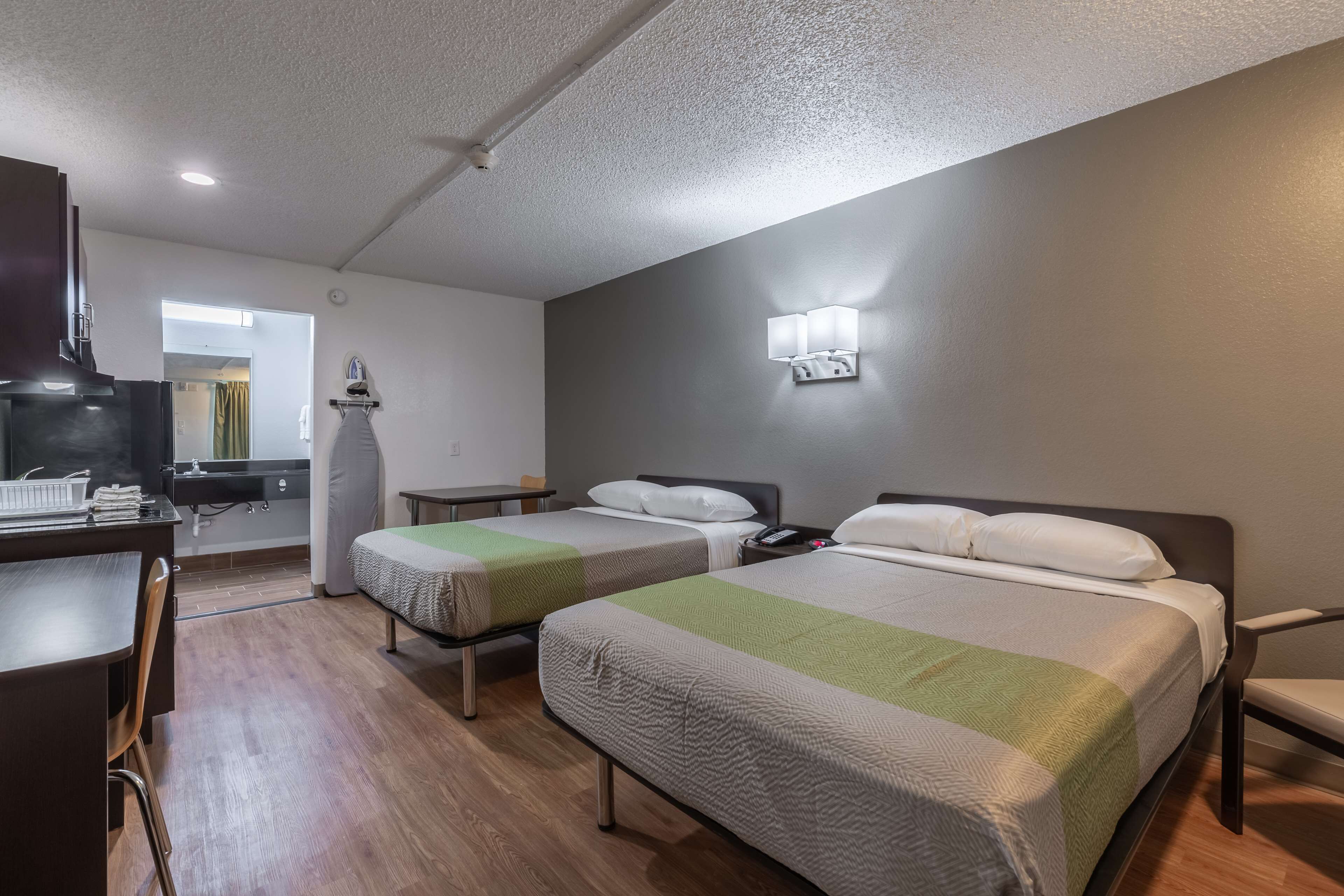 Habitación de hotel con dos camas, un escritorio, una silla, un televisor y un baño visible a través de una puerta abierta.