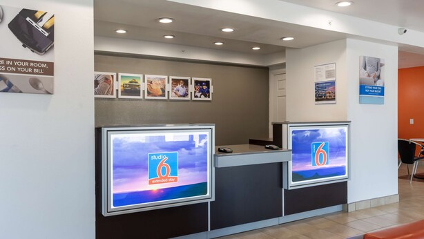 Un área de recepción con dos pantallas digitales grandes, un mostrador de recepción y una zona de estar con sillas naranjas.
