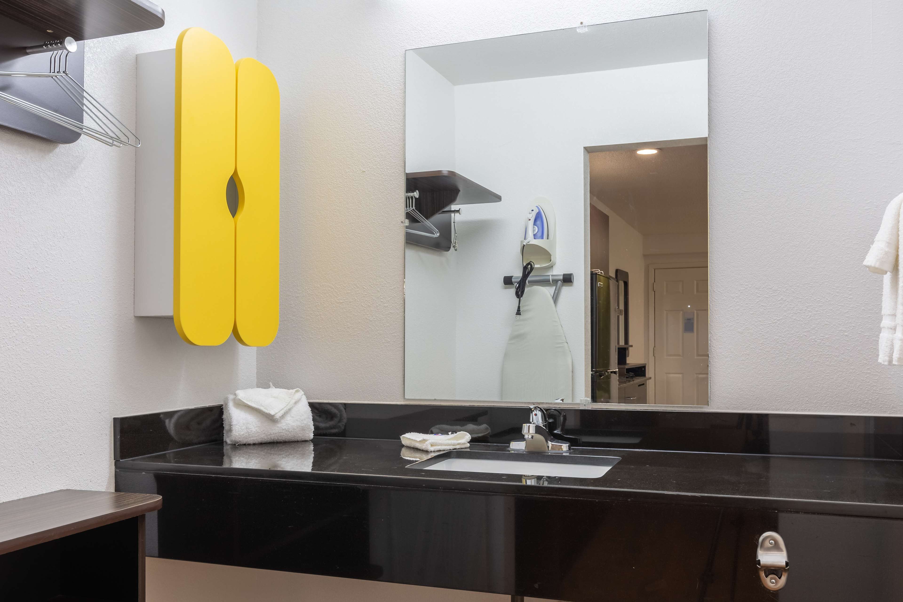 Un baño moderno con encimera negra, un espejo grande y un perchero amarillo.
