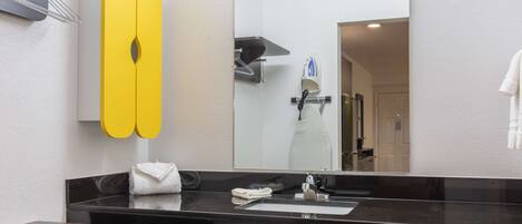 A modern bathroom with a black countertop, a large mirror, and a yellow towel rack.