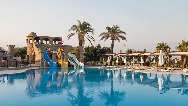 A swimming pool with a water slide, palm trees, and lounge chairs. - Club Hotel Felicia Village - All Inclusive (Manavgat)