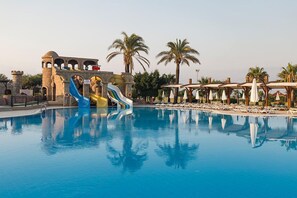 A swimming pool with a water slide, palm trees, and lounge chairs. - Club Hotel Felicia Village - All Inclusive (Manavgat)