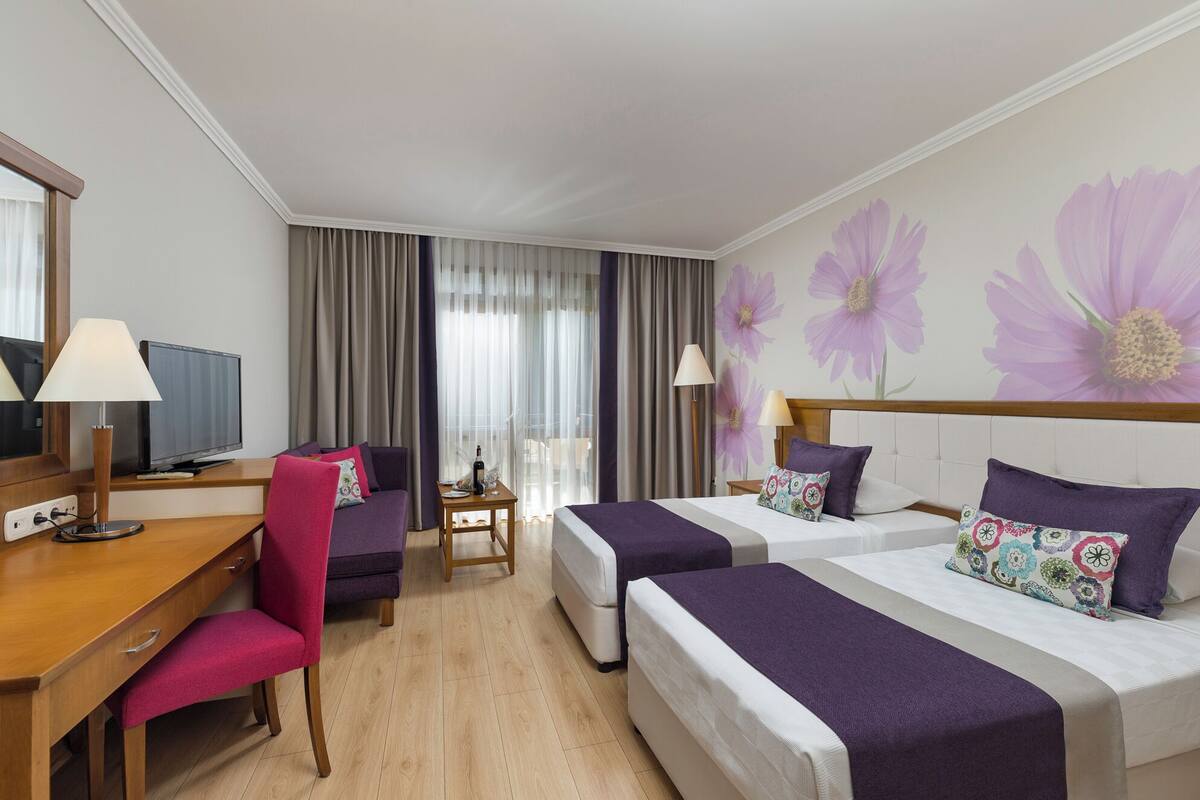 A hotel room with two beds, a desk, a chair, a TV, and a window with curtains.