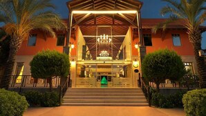 A hotel entrance with a covered walkway, palm trees, and a reception area. - Club Hotel Felicia Village - All Inclusive (Manavgat)