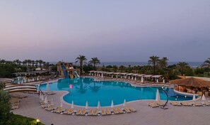 A large pool with a water slide, surrounded by lounge chairs and umbrellas, with a view of the ocean. - Club Hotel Felicia Village - All Inclusive (Manavgat)