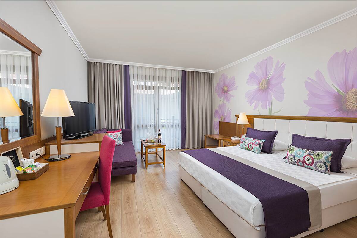 A hotel room with a bed, desk, chair, television, and a large mirror.