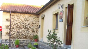 Un edificio con fachada de piedra, tejado de tejas y una pequeña escalera que conduce a una puerta. Hay varias plantas en macetas en los escalones y en el suelo.