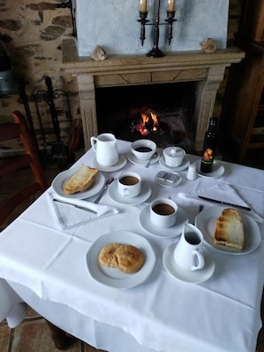 A breakfast setup with bread, coffee, and a bottle of wine on a table in front of a fireplace.