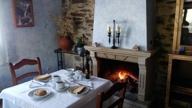 Una mesa de comedor dispuesta con platos, tazas y un candelabro en una habitación con pared de piedra y chimenea.