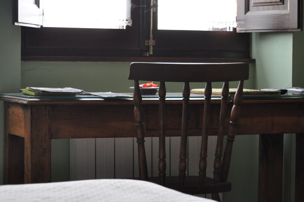 A wooden chair at a table with papers and a bowl of fruit.