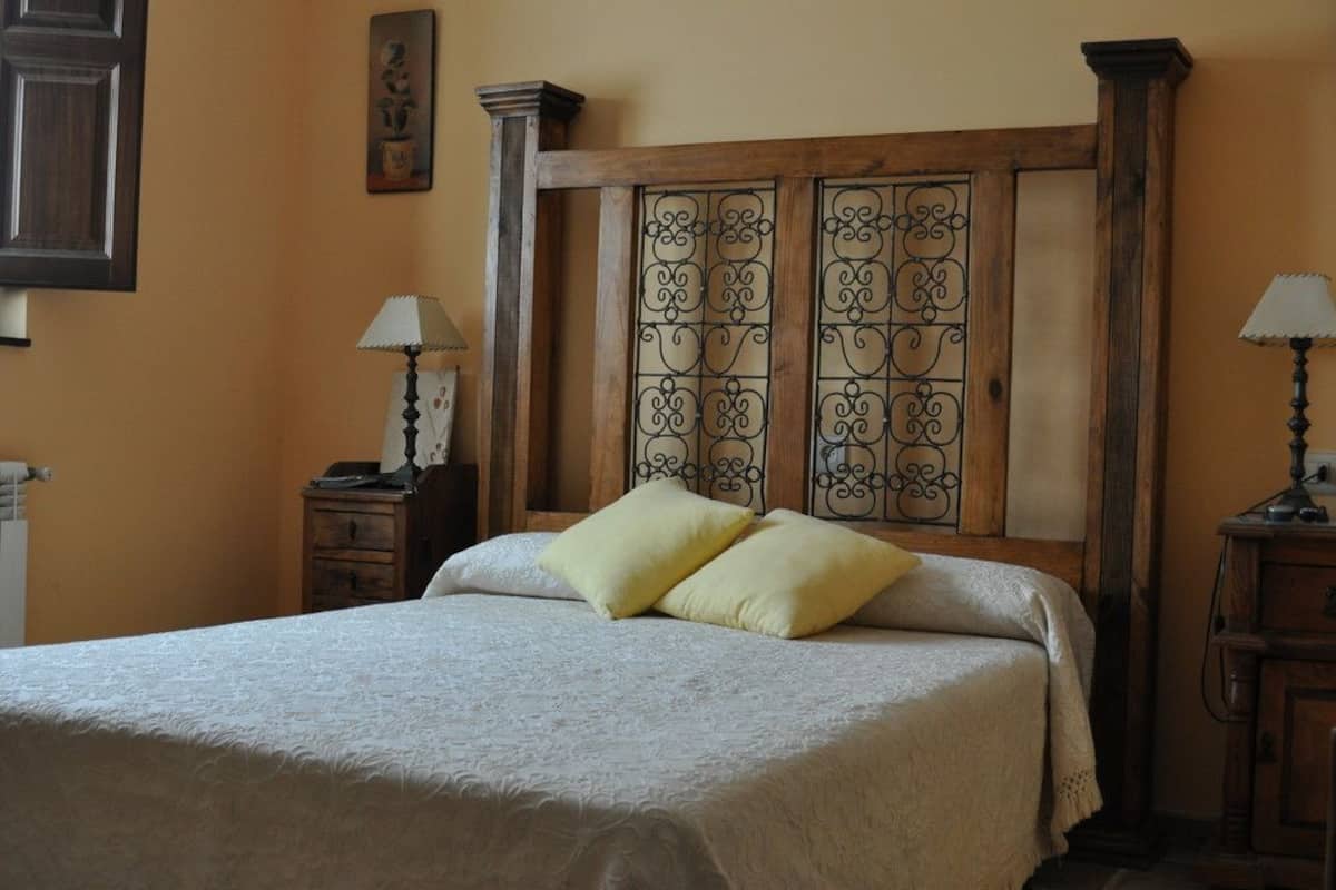 Una cama bien tendida con dos almohadas, un cabecero de madera con paneles metálicos decorativos y dos mesitas de noche con lámparas.