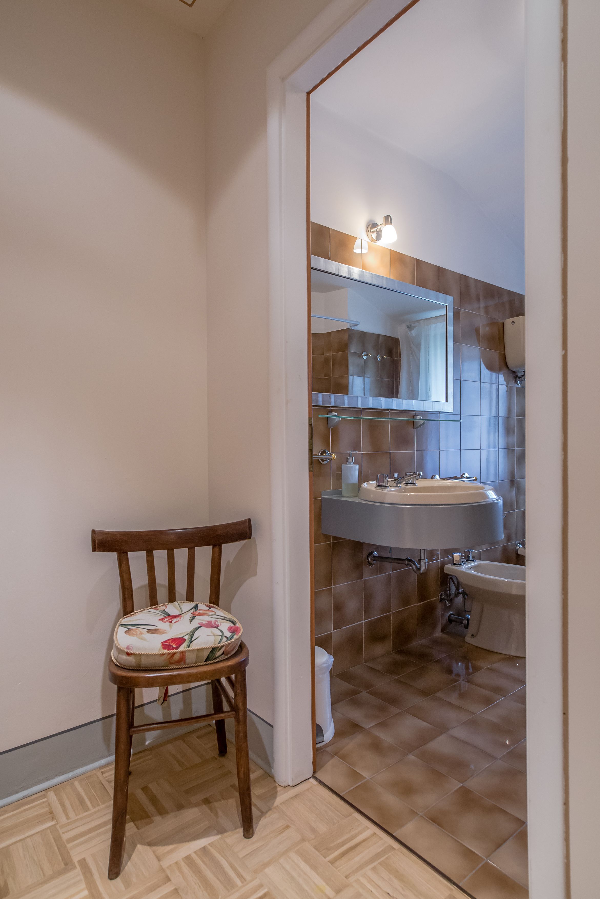 A bathroom with a wooden chair, a sink, and a mirror.