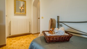A room with a bed, a wicker basket with towels, a mirror, and a radiator. - Agriturismo Il Quercione (Assisi)