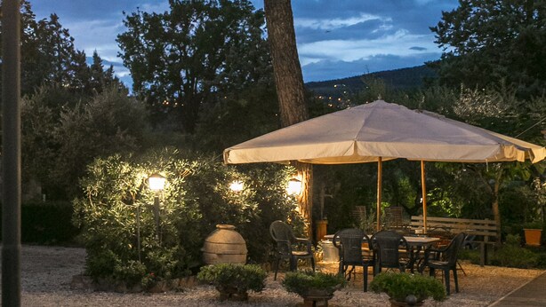 An outdoor patio area with a large umbrella, seating, and a well-lit environment. - Agriturismo Il Quercione (Assisi)