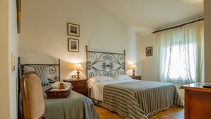 A bedroom with a bed, two bedside tables, a chair, a wooden floor, and a window with curtains. - Agriturismo Il Quercione (Assisi)