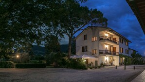 A two-story building with a balcony, outdoor seating, and a well-lit entrance. - Agriturismo Il Quercione (Assisi)