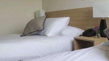 Habitación de hotel con dos camas, una mesita de noche con lámpara y teléfono.