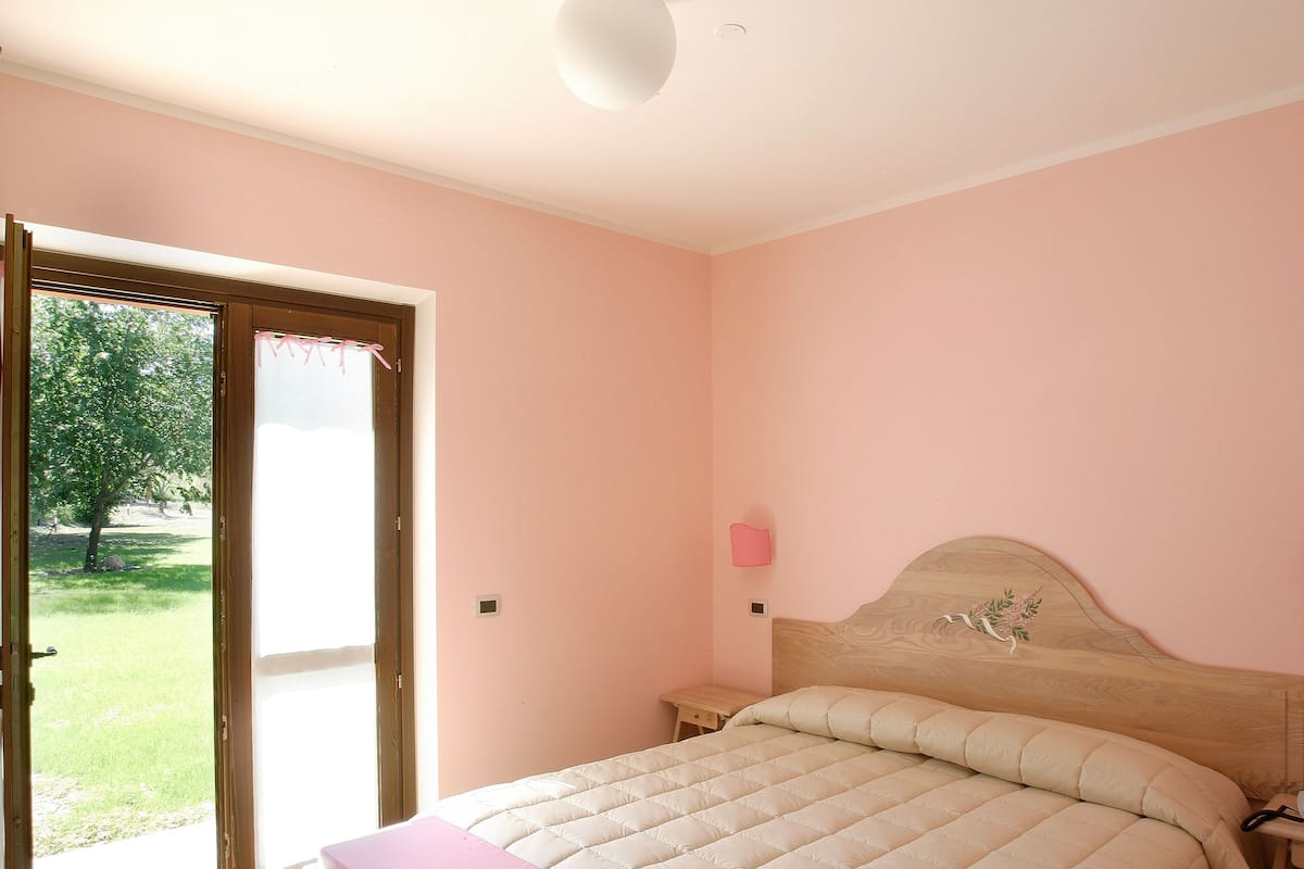 A bedroom with a bed, two bedside tables, a nightstand, a window, and a door leading to a garden.