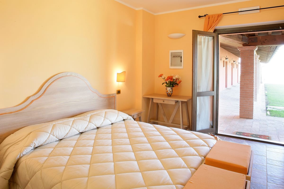 A bedroom with a bed, a bedside table, a desk, and a view of the outside.