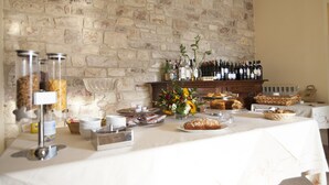 A breakfast buffet with various food items and beverages, set against a stone wall backdrop. - Country House Poggio Fiorito (Assisi)