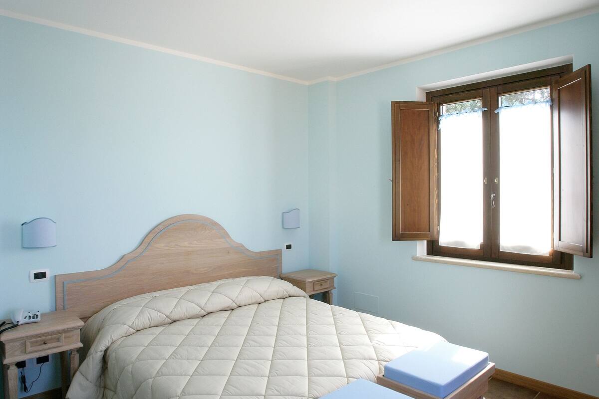 A bedroom with a bed, bedside tables, a nightstand, a window, and a ceiling light.