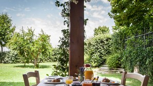 An outdoor dining table set with breakfast items, surrounded by lush greenery and a wooden post. - Country House Poggio Fiorito (Assisi)