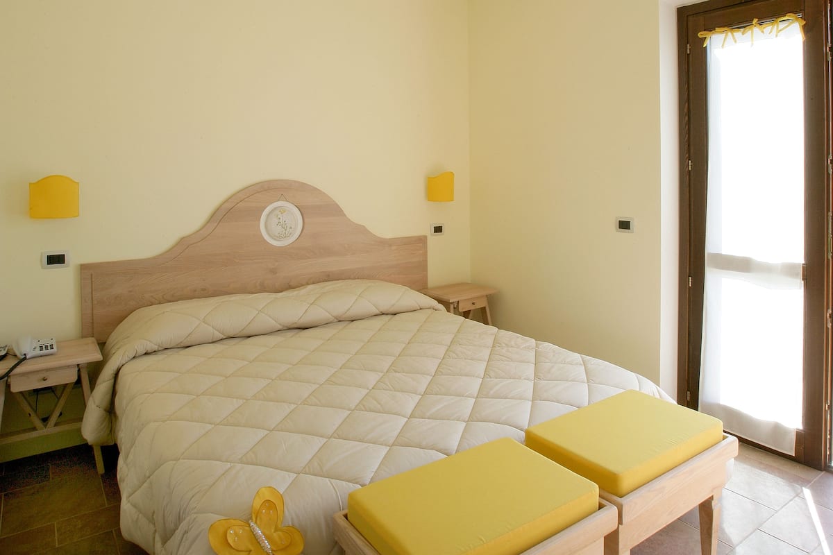 A bedroom with a bed, bedside tables, a wooden bench, and a door leading to a balcony.