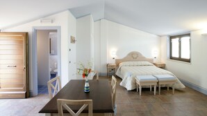 A bedroom with a bed, bedside tables, a nightstand, a wooden table with chairs, and a vase with flowers. - Country House Poggio Fiorito (Assisi)