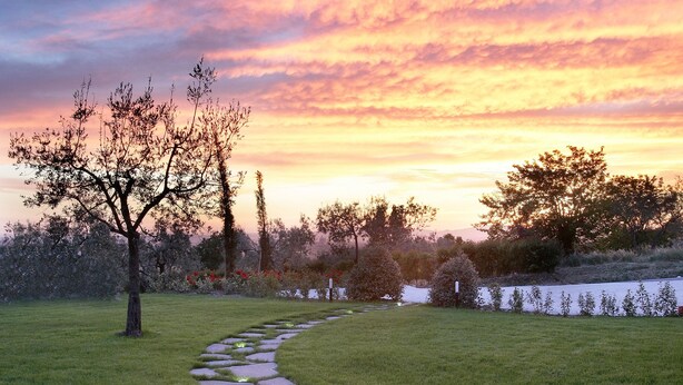 A stone pathway in a grassy area with trees and a sunset in the background. - Country House Poggio Fiorito (Assisi)