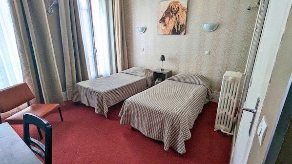 Una habitación con dos camas, una silla, una mesa, un radiador y un cuadro en la pared.