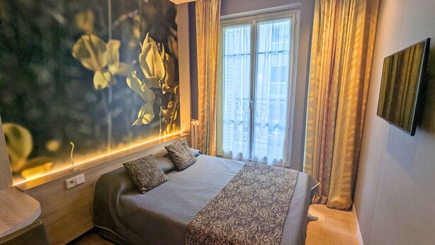 Habitación de hotel con cama, un amplio ventanal con cortinas, televisor montado en la pared y un adorno decorativo.