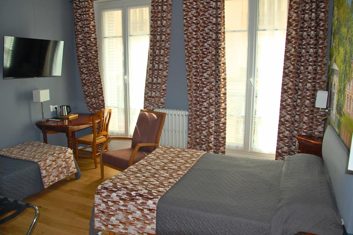 A hotel room with two single beds, a desk, a chair, a TV, and a radiator.