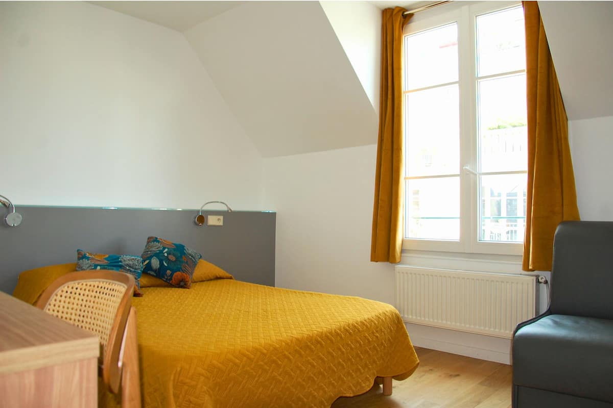 A bedroom with a bed, a chair, a radiator, and a window with curtains.