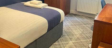 A hotel room with a bed, a wooden wardrobe, a desk, and a window with curtains.