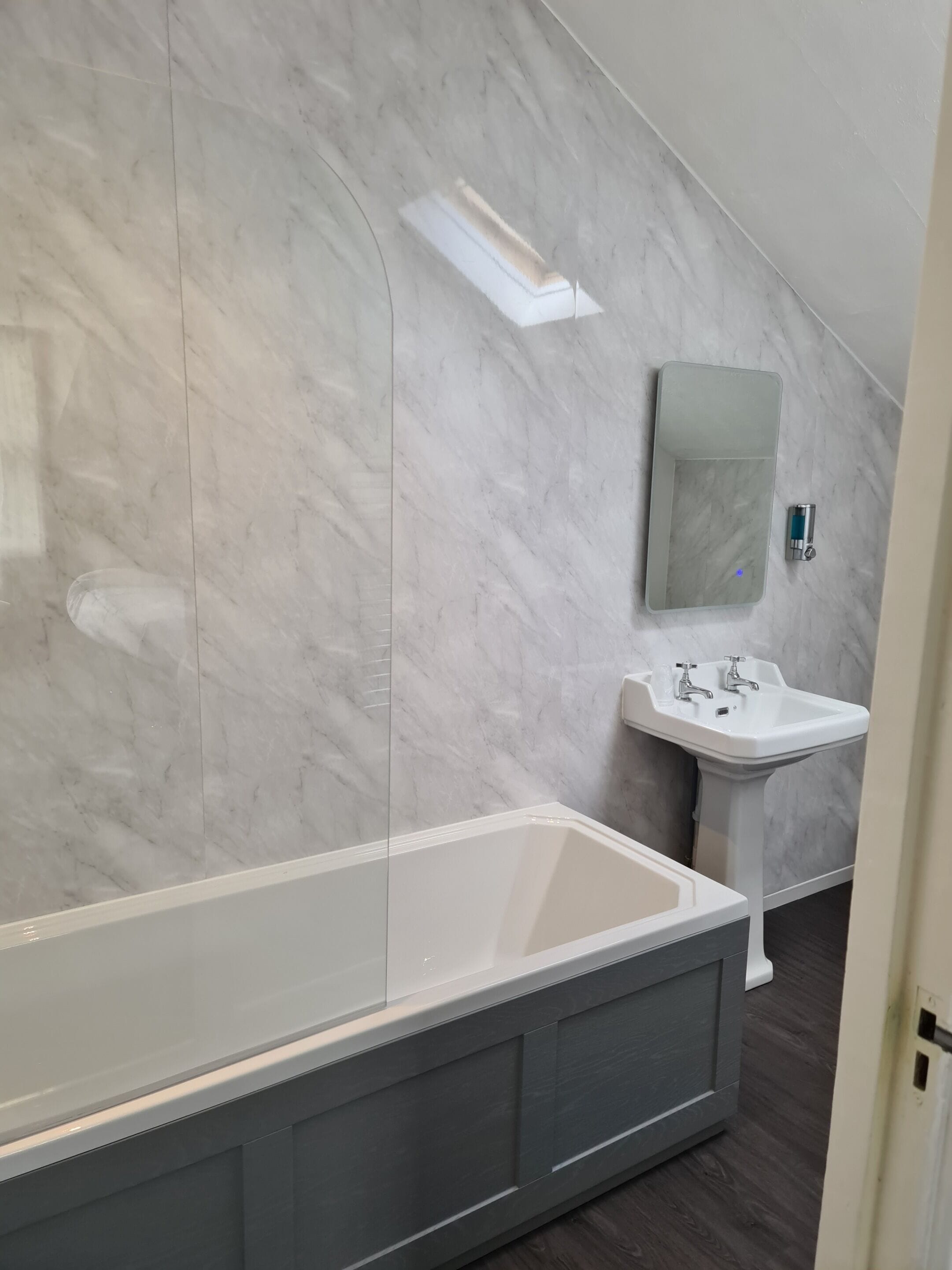A modern bathroom with a large bathtub, a pedestal sink, and a mirror above the sink.