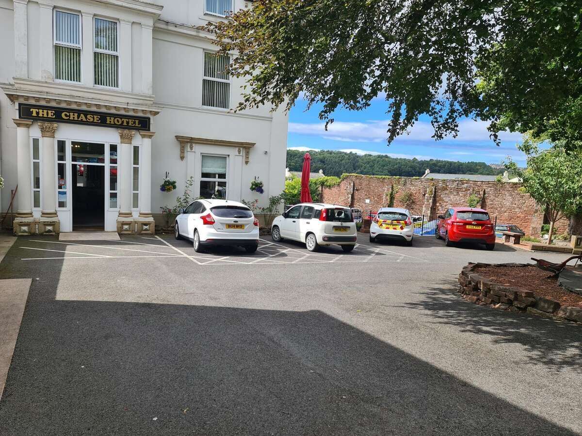 The Chase Hotel with a parking area, a brick wall, and a view of the countryside.