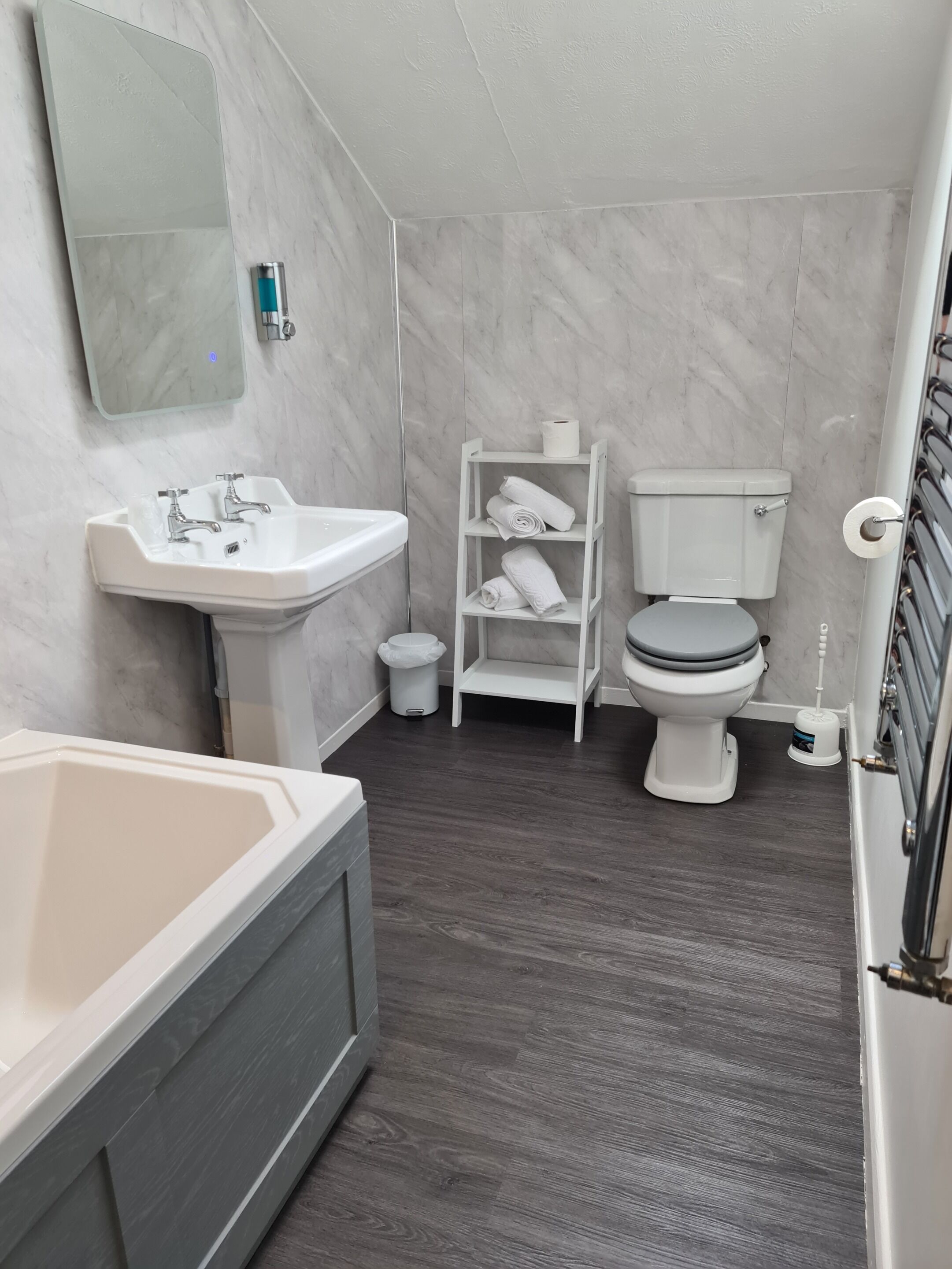 A bathroom with a bathtub, sink, toilet, and a shelf with towels.