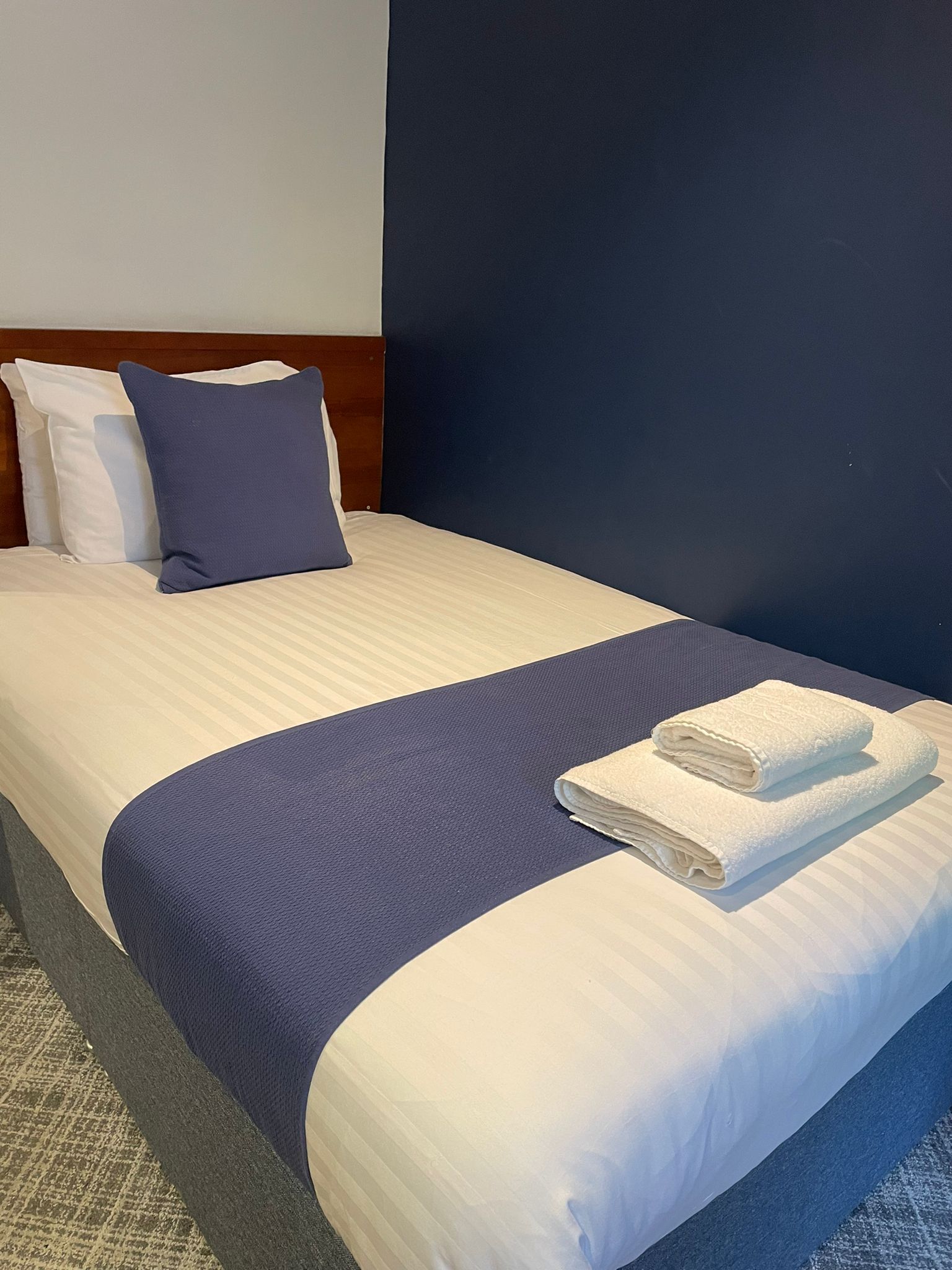Una cama bien hecha con ropa de cama blanca y azul, una toalla blanca doblada y un cabecero de madera.