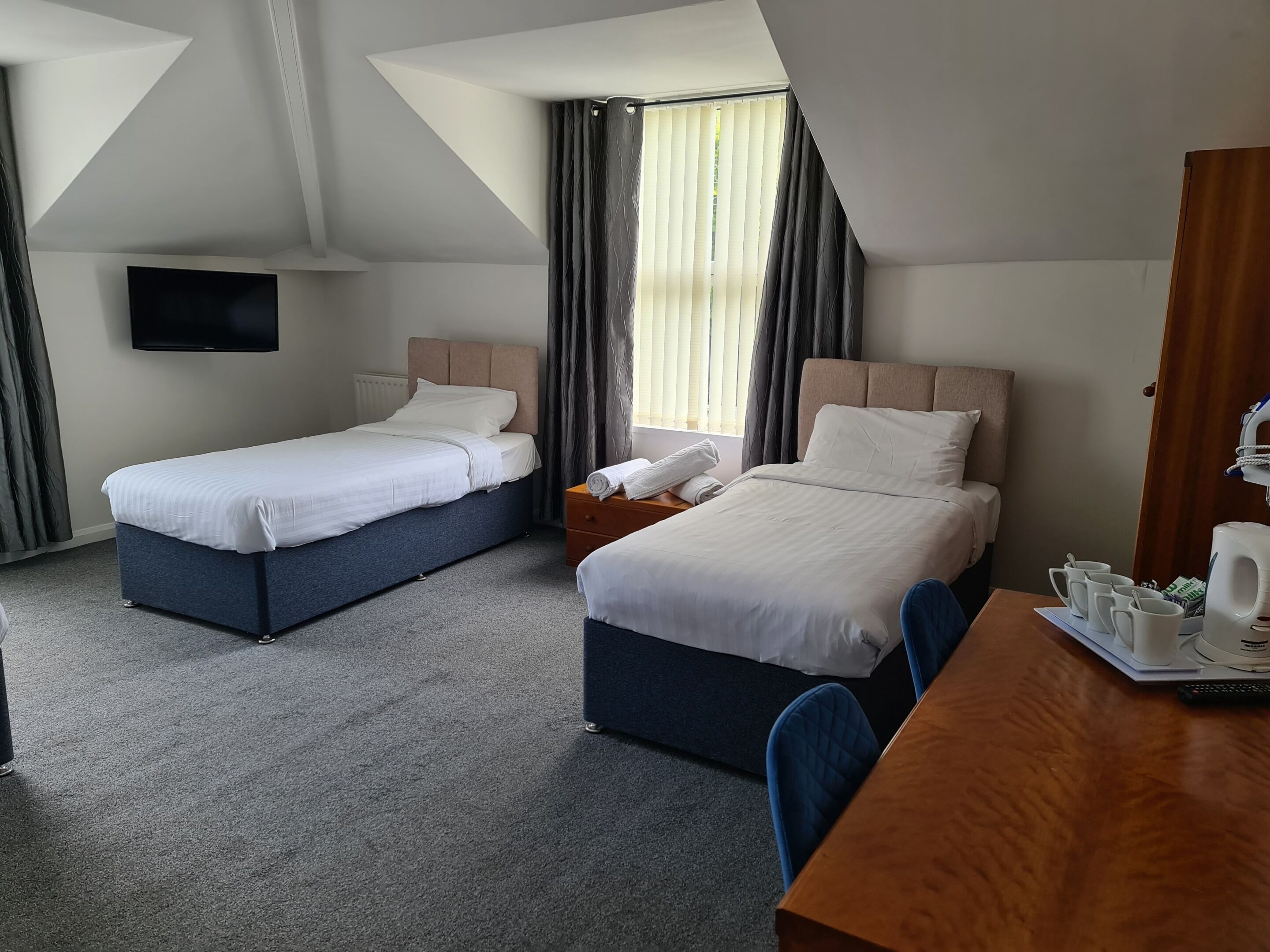 Een hotelkamer met twee bedden, een televisie, een bureau met koffiezetapparaat en een raam met gordijnen.