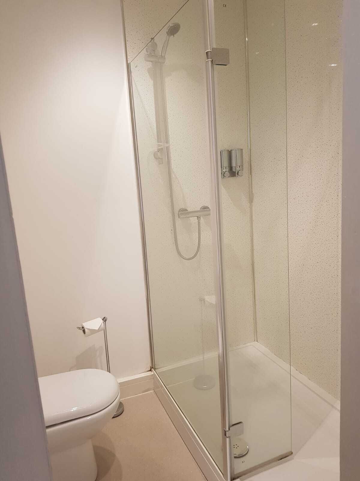 A glass-enclosed shower stall with a handheld showerhead and a wall-mounted control panel.