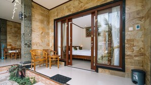 A spacious room with a large sliding glass door leading to a balcony, wooden furniture, and a bed with a white headboard. - Sari Nusa Inn (Lembongan Island)