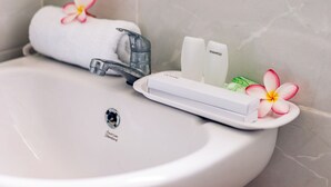 A bathroom sink with a handheld showerhead, a towel, and toiletries. - Sari Nusa Inn (Lembongan Island)