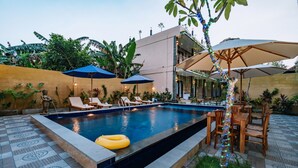 A swimming pool with lounge chairs and umbrellas, surrounded by greenery and a tiled patio. - Sari Nusa Inn (Lembongan Island)