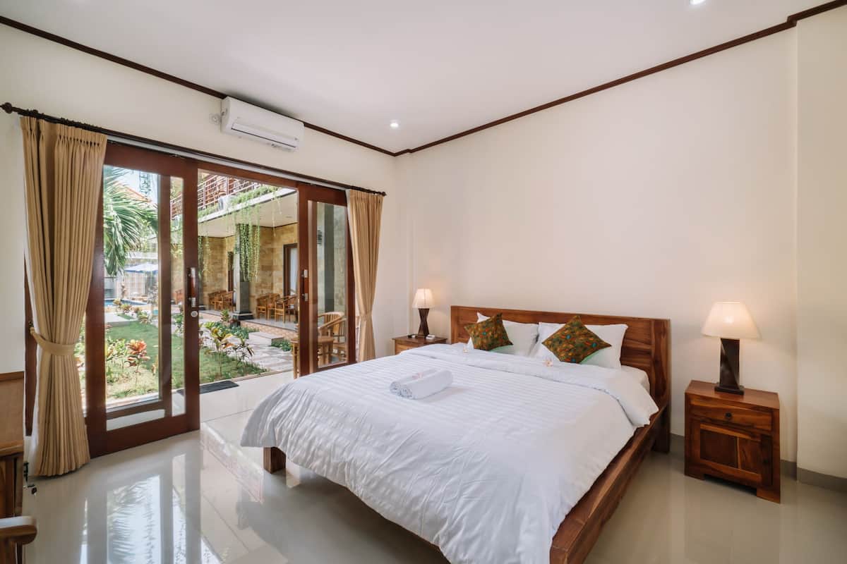A bedroom with a large bed, wooden headboard, two bedside tables with lamps, and a sliding glass door leading to an outdoor area.