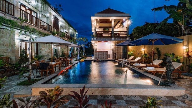 A pool area with lounge chairs and umbrellas, surrounded by plants and a building with multiple floors and balconies. - Sari Nusa Inn (Lembongan Island)