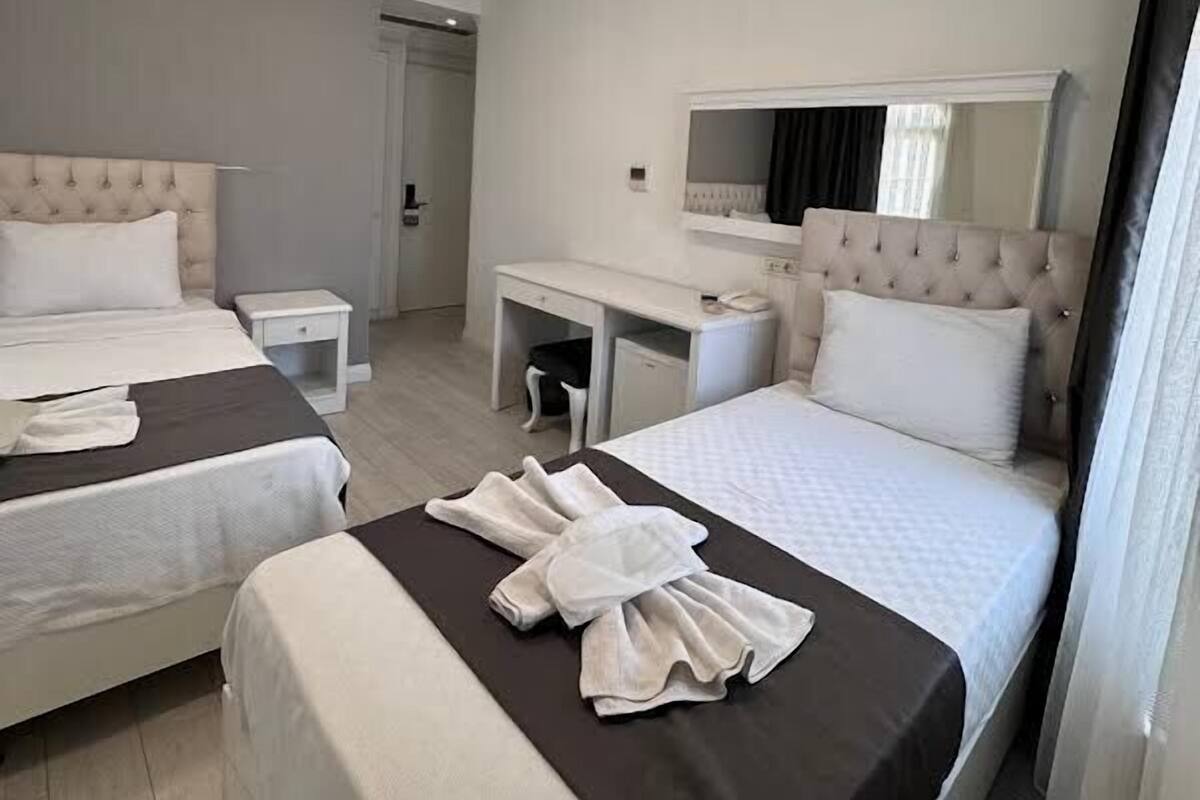 A hotel room with two beds, a desk, a mirror, and a wardrobe.