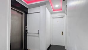 Un pasillo con piso negro brillante, paredes blancas y una puerta con ascensor metálico.