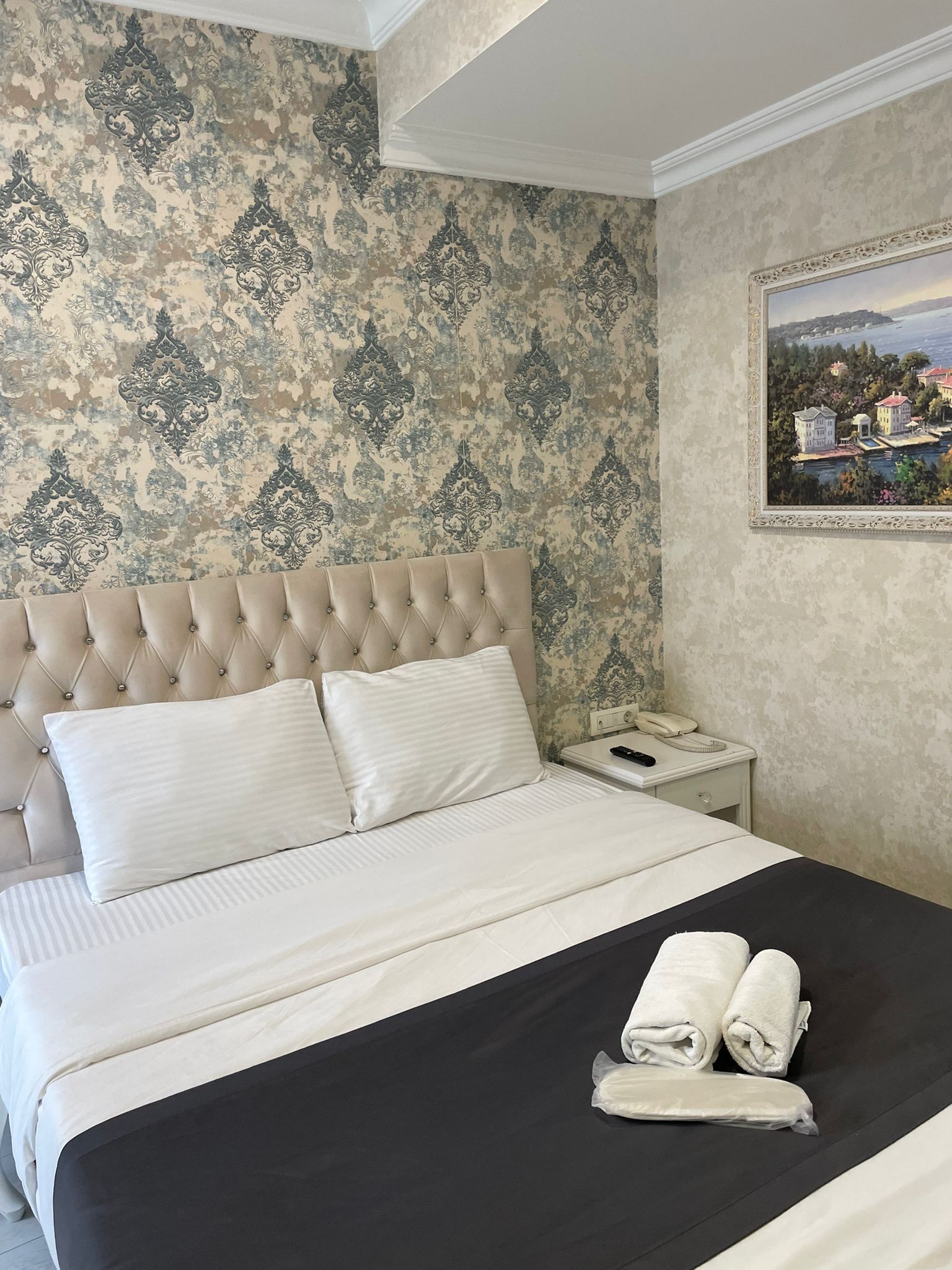 A neatly made bed with a tufted headboard, white bedding, and two rolled towels on the bed.